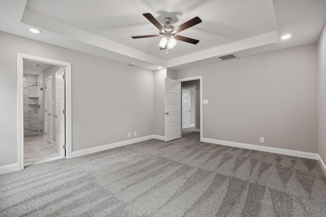 unfurnished bedroom with ceiling fan, light colored carpet, connected bathroom, and a raised ceiling