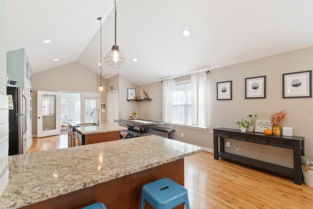 kitchen featuring light stone counters, light hardwood / wood-style flooring, lofted ceiling, decorative light fixtures, and a kitchen island with sink