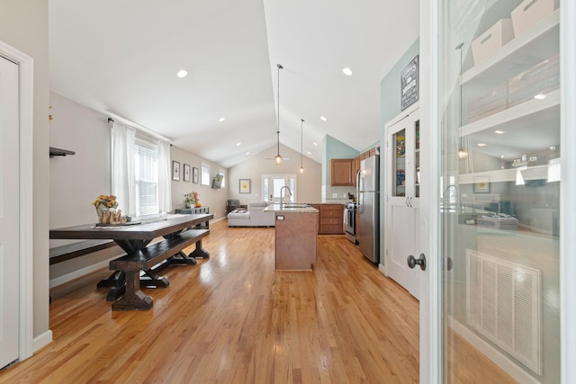 kitchen featuring sink, stainless steel appliances, light hardwood / wood-style flooring, an island with sink, and lofted ceiling