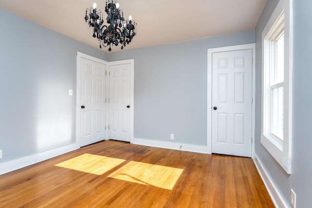 unfurnished room featuring wood-type flooring, a healthy amount of sunlight, and a notable chandelier