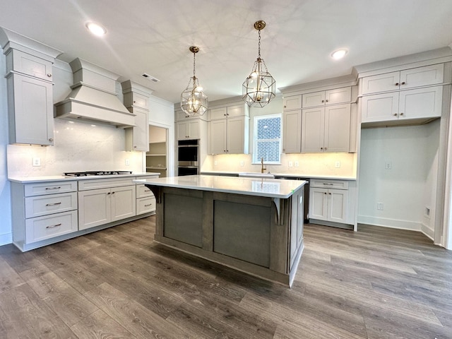 kitchen with gas stovetop, stainless steel double oven, a kitchen island, a sink, and premium range hood