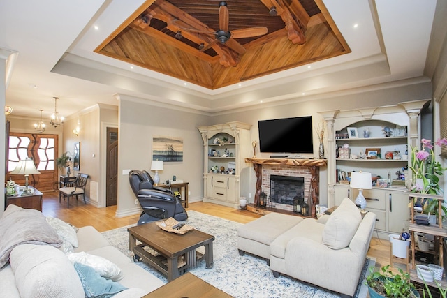 living room featuring crown molding, light hardwood / wood-style flooring, a tray ceiling, a fireplace, and ceiling fan with notable chandelier