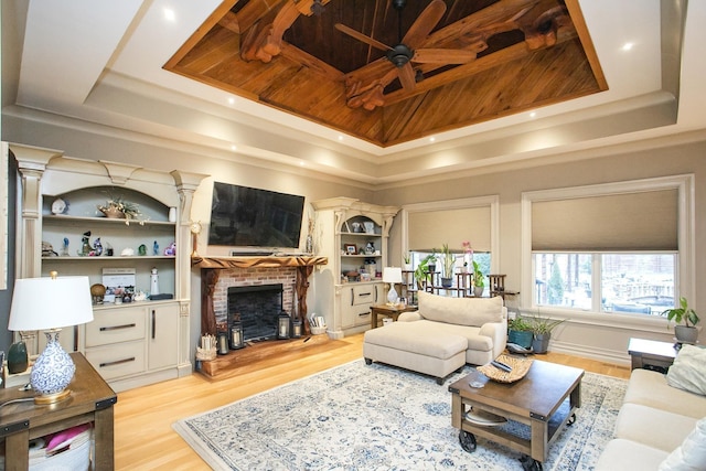 living room with ceiling fan, light hardwood / wood-style flooring, a fireplace, and a tray ceiling