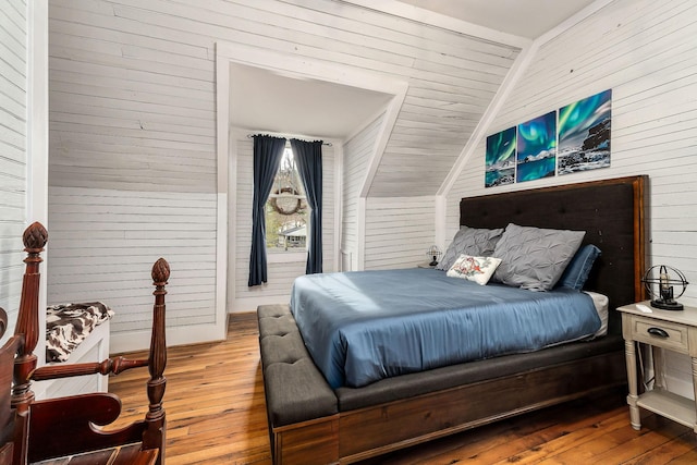 bedroom with hardwood / wood-style floors, wooden walls, and vaulted ceiling