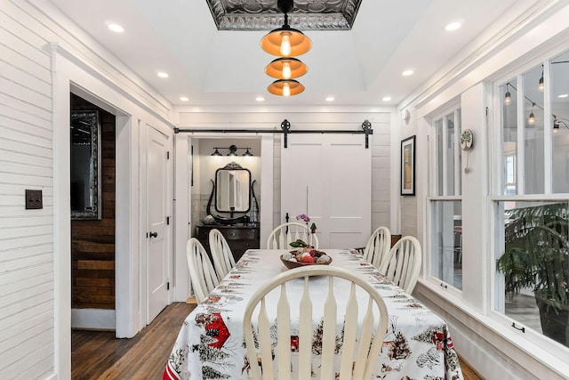 dining space featuring a barn door, dark hardwood / wood-style flooring, and a tray ceiling