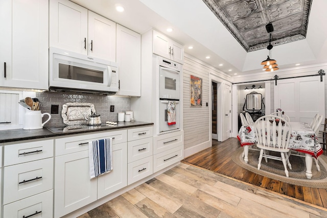 kitchen with light wood-type flooring, white appliances, a raised ceiling, a barn door, and white cabinetry