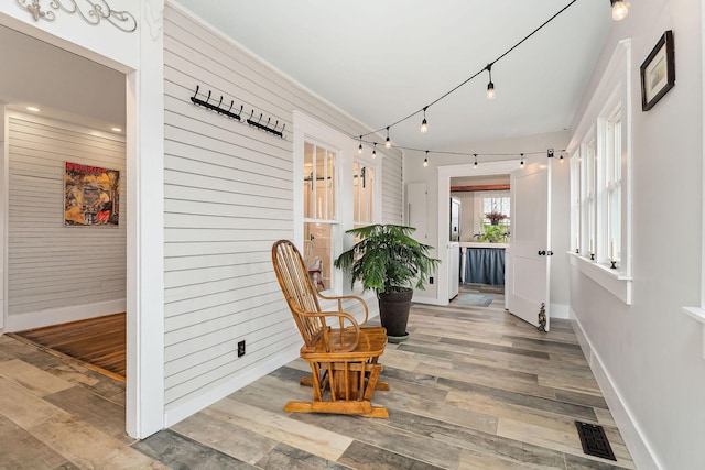 sitting room featuring hardwood / wood-style flooring, ornamental molding, rail lighting, and wooden walls