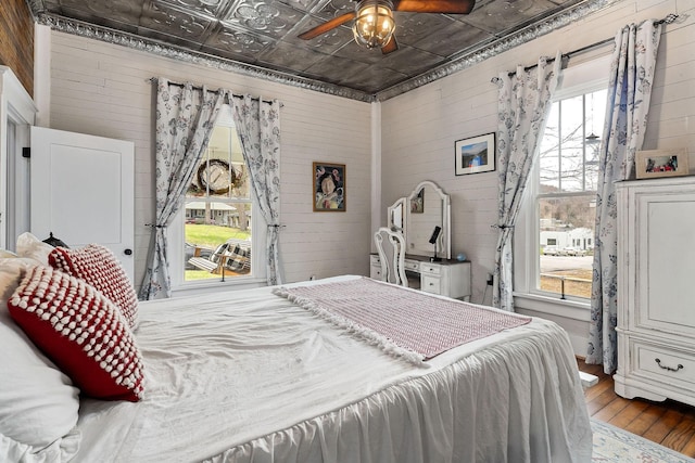 bedroom with hardwood / wood-style flooring, multiple windows, wooden walls, and ceiling fan