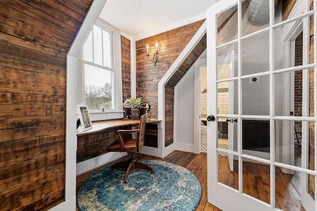 office area featuring hardwood / wood-style floors, wood walls, lofted ceiling, french doors, and built in desk