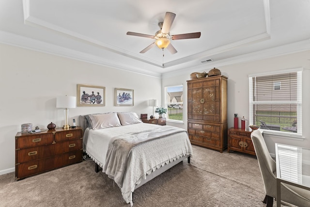 carpeted bedroom featuring ceiling fan, ornamental molding, a tray ceiling, and multiple windows