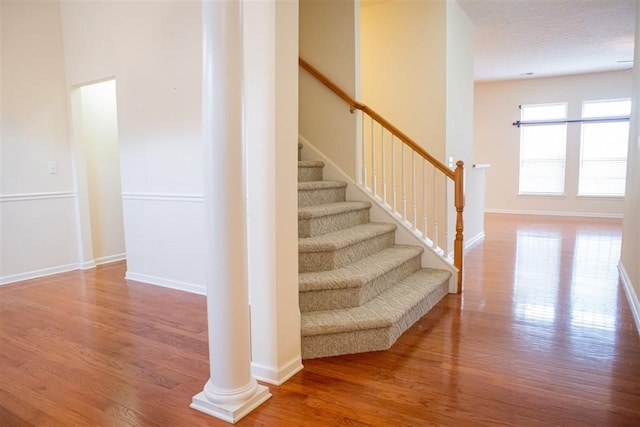 staircase featuring wood-type flooring, a textured ceiling, and decorative columns