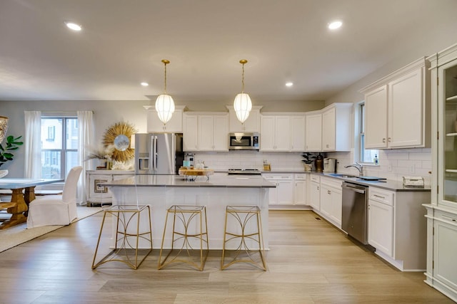 kitchen with appliances with stainless steel finishes, a center island, light hardwood / wood-style flooring, and pendant lighting