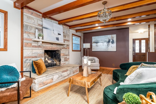 living room with beam ceiling, a stone fireplace, hardwood / wood-style floors, and an inviting chandelier