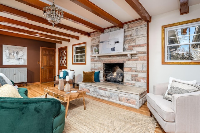 living room with beam ceiling, a stone fireplace, wood-type flooring, and a notable chandelier