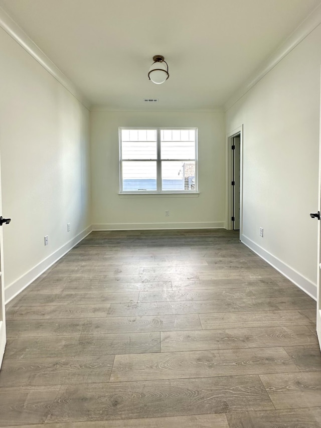 spare room with baseboards, visible vents, ornamental molding, and wood finished floors