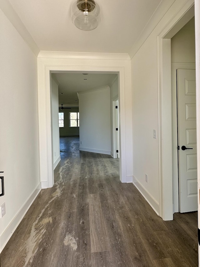 corridor featuring dark wood-style floors, ornamental molding, and baseboards