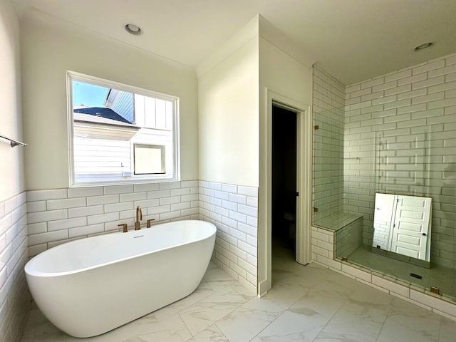 bathroom featuring marble finish floor, a wainscoted wall, a freestanding bath, toilet, and a shower stall