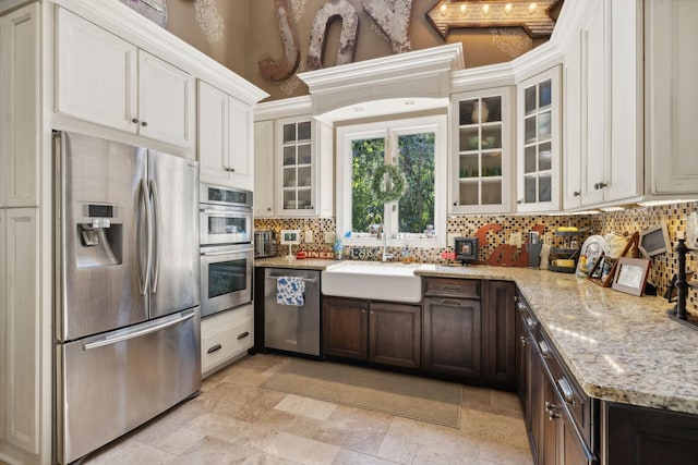 kitchen featuring appliances with stainless steel finishes, light stone counters, dark brown cabinets, and sink