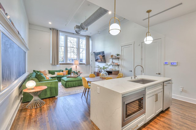 kitchen featuring sink, stainless steel appliances, light stone counters, decorative light fixtures, and a center island with sink