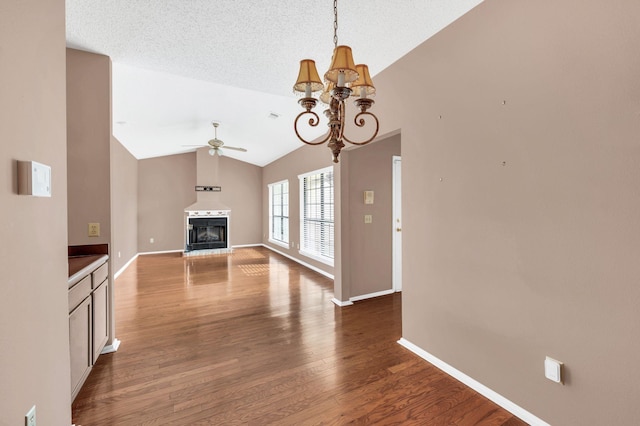 unfurnished living room featuring a textured ceiling, ceiling fan with notable chandelier, dark wood-type flooring, and vaulted ceiling