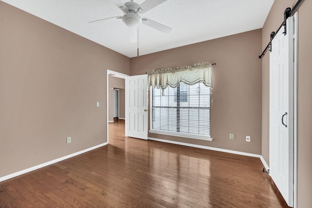 spare room featuring dark hardwood / wood-style floors, a barn door, a textured ceiling, and ceiling fan