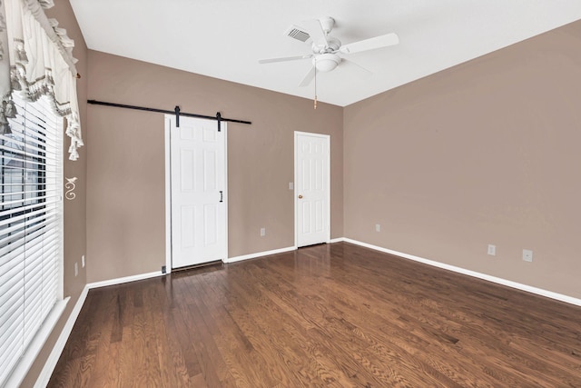 unfurnished bedroom featuring ceiling fan, a barn door, and dark wood-type flooring