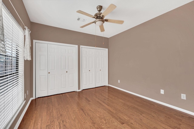 unfurnished bedroom with wood-type flooring, two closets, and ceiling fan