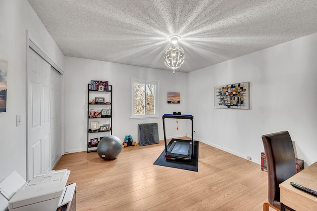 exercise area featuring light wood-type flooring, a chandelier, and a textured ceiling