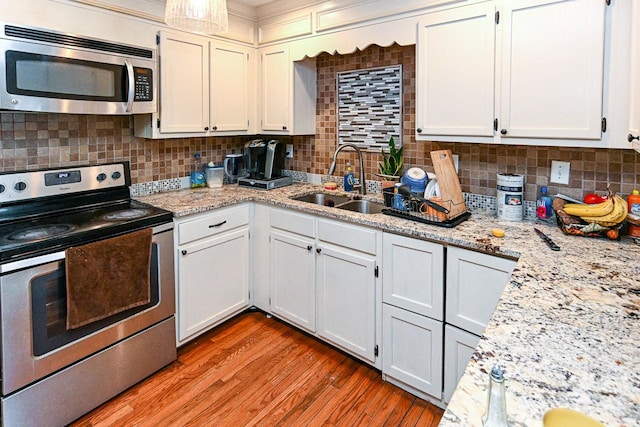 kitchen with appliances with stainless steel finishes, white cabinetry, sink, decorative backsplash, and light hardwood / wood-style flooring