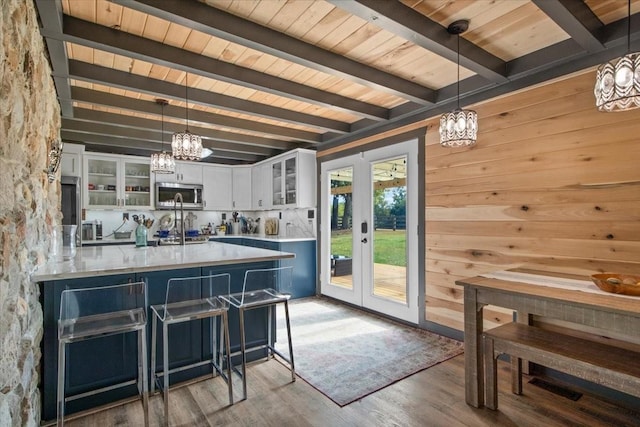 kitchen with wood walls, wood-type flooring, white cabinetry, and hanging light fixtures