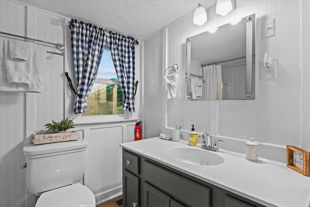 bathroom featuring wood walls, vanity, a textured ceiling, and toilet