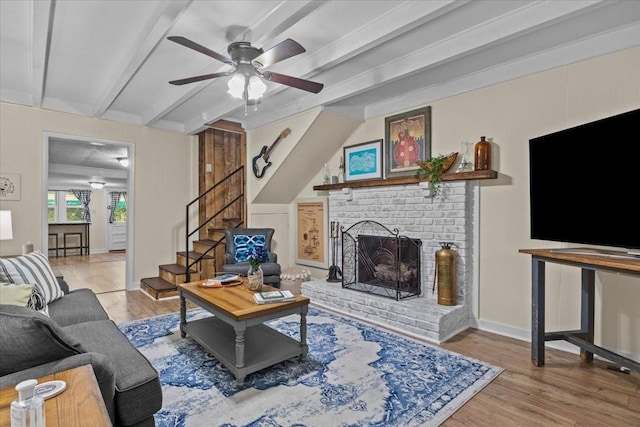 living room with beam ceiling, light wood-type flooring, a brick fireplace, and ceiling fan