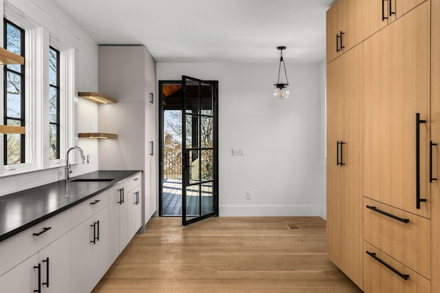 kitchen with sink, light brown cabinets, light hardwood / wood-style flooring, pendant lighting, and white cabinets