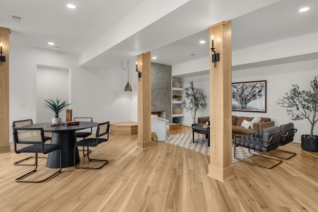 dining space with built in features, a fireplace, light hardwood / wood-style floors, and decorative columns