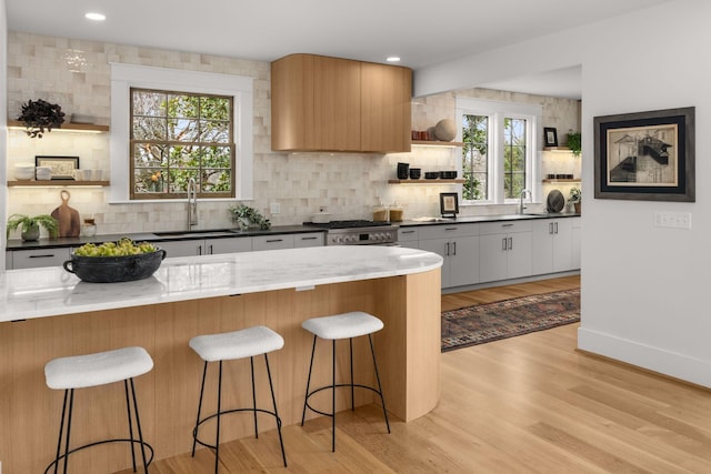 kitchen featuring sink, a kitchen bar, tasteful backsplash, stainless steel range oven, and white cabinets