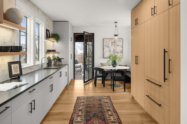 kitchen featuring sink, hanging light fixtures, breakfast area, light brown cabinets, and light wood-type flooring