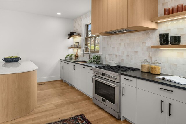 kitchen featuring sink, high end range, light wood-type flooring, custom range hood, and white cabinets