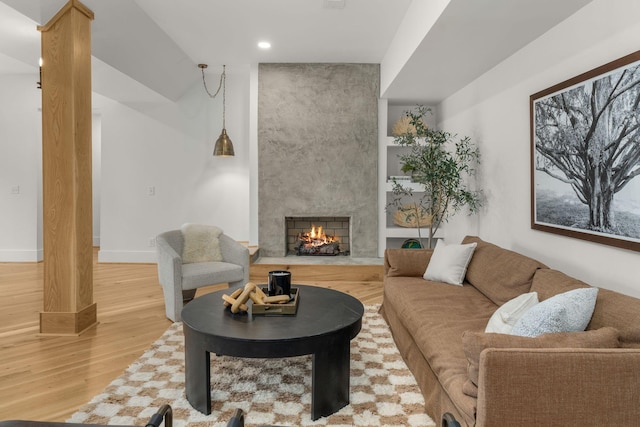 living room with wood-type flooring, a large fireplace, and ornate columns