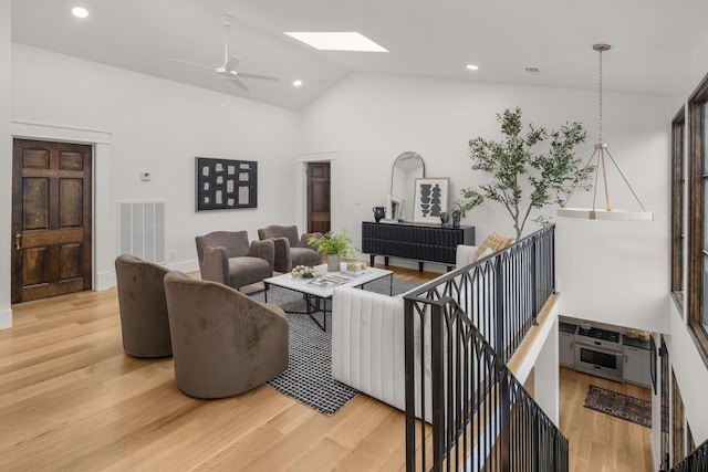 living room with high vaulted ceiling, hardwood / wood-style floors, ceiling fan, and a skylight