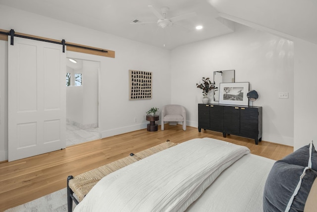 bedroom with hardwood / wood-style flooring, ceiling fan, and a barn door