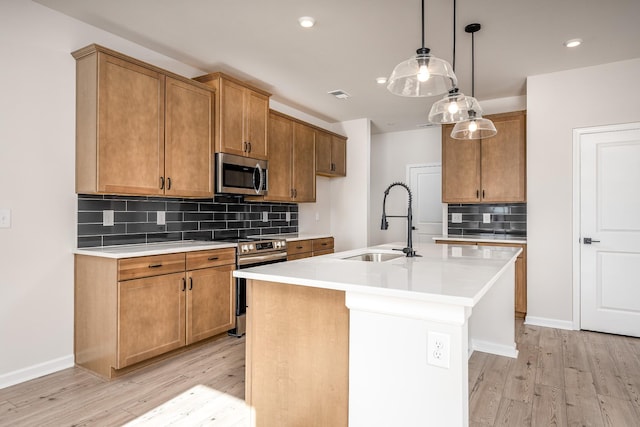 kitchen with a center island with sink, sink, hanging light fixtures, light hardwood / wood-style floors, and stainless steel appliances