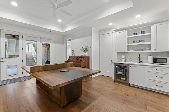 kitchen with wine cooler, white cabinetry, crown molding, a tray ceiling, and hardwood / wood-style floors