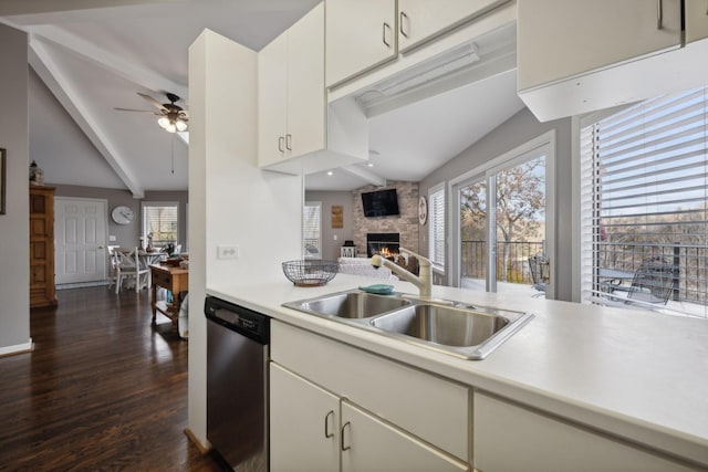 kitchen featuring stainless steel dishwasher, sink, lofted ceiling with beams, dark hardwood / wood-style floors, and a stone fireplace