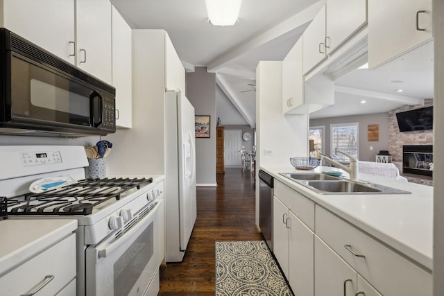 kitchen with white cabinetry, sink, a stone fireplace, dark hardwood / wood-style flooring, and white appliances