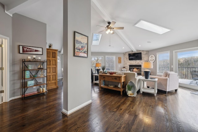 living room with a skylight, dark hardwood / wood-style floors, ceiling fan, a fireplace, and beam ceiling