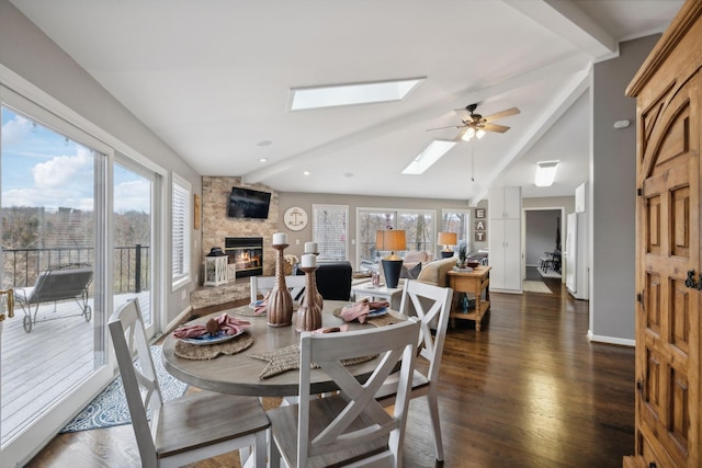 dining space with a fireplace, ceiling fan, dark wood-type flooring, and vaulted ceiling with skylight