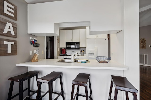 kitchen featuring white cabinets, sink, dark hardwood / wood-style floors, white fridge with ice dispenser, and kitchen peninsula