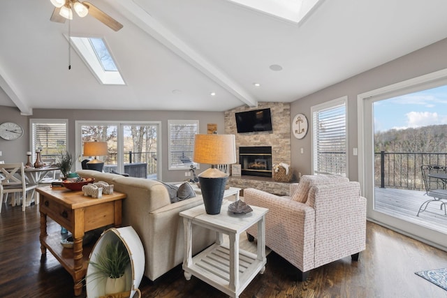 living room featuring lofted ceiling with skylight, a fireplace, ceiling fan, and dark wood-type flooring