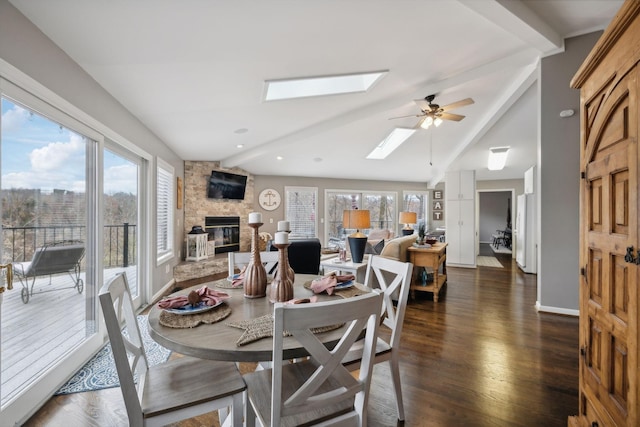 dining room featuring vaulted ceiling with skylight, dark hardwood / wood-style floors, ceiling fan, and a stone fireplace