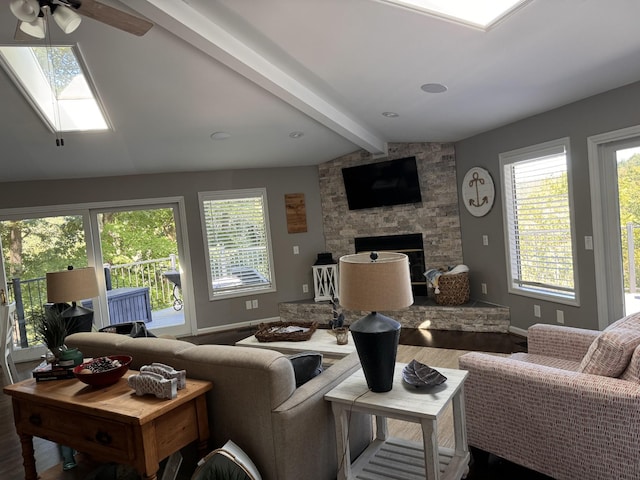 living room featuring a fireplace, ceiling fan, hardwood / wood-style floors, and vaulted ceiling with skylight